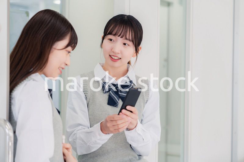 教室でスマホを見ながら話す女子高生