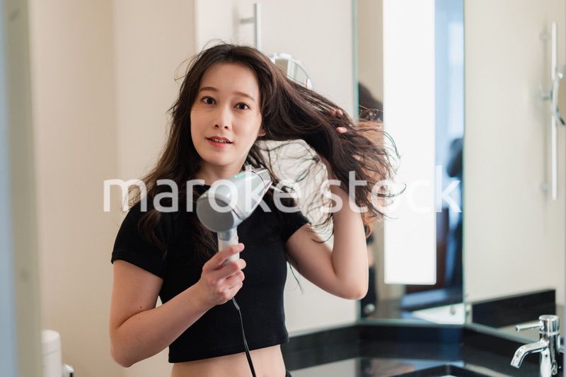 ドライヤーで髪を乾かす若い女性