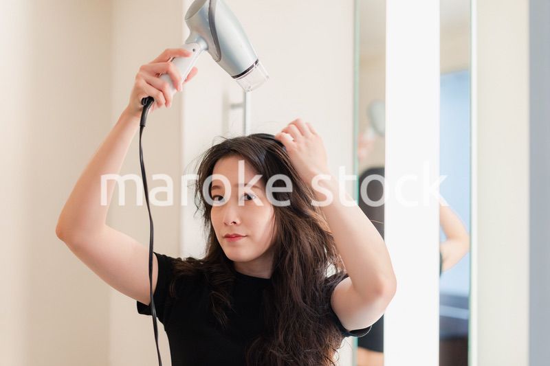 ドライヤーで髪を乾かす若い女性