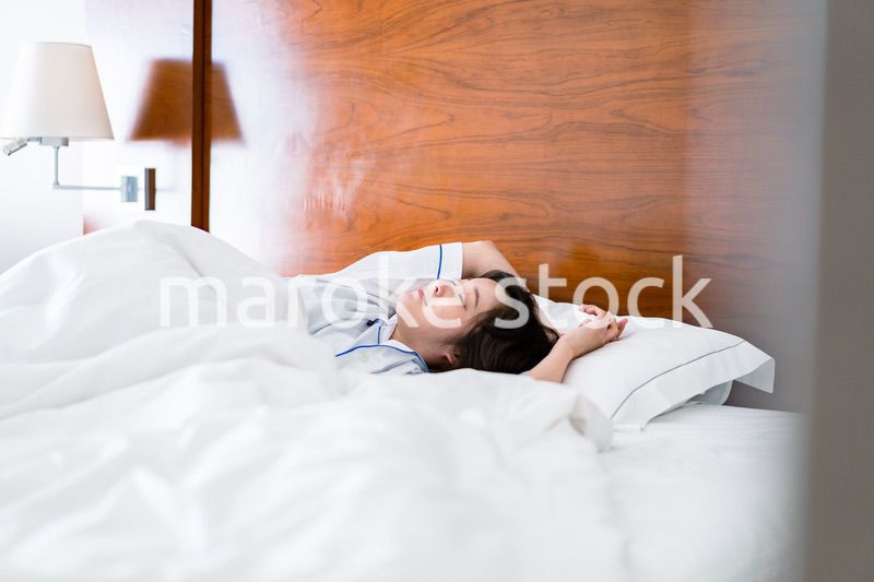 明るい時間にベッドで寝る若い女性