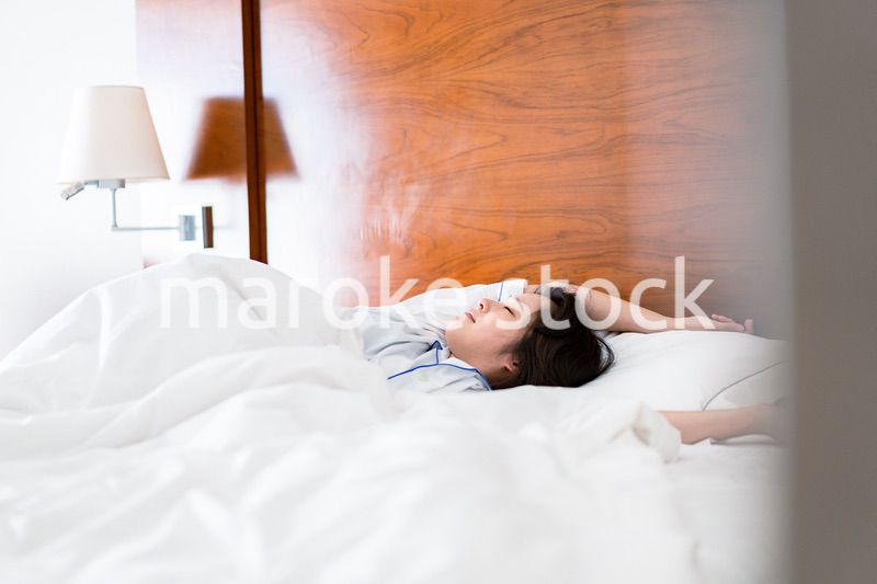 明るい時間にベッドで寝る若い女性
