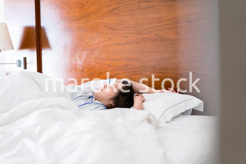 明るい時間にベッドで寝る若い女性