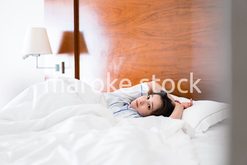 明るい時間にベッドで寝る若い女性
