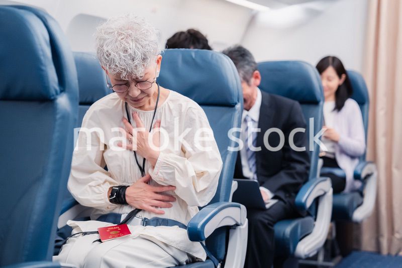 飛行機の機内で体調不良に苦しむ高齢の女性