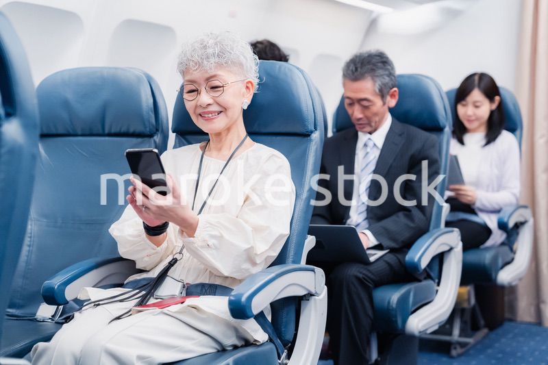 飛行機でスマホを使うシニア女性