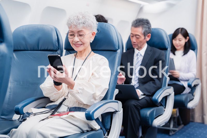 飛行機でスマホを使うシニア女性