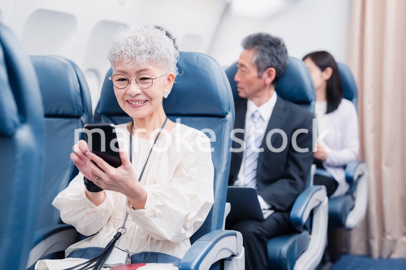 飛行機でスマホを使うシニア女性