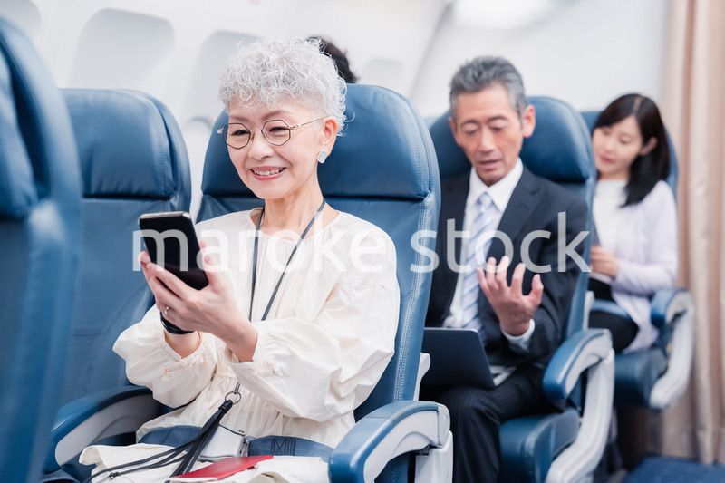飛行機でスマホを使うシニア女性