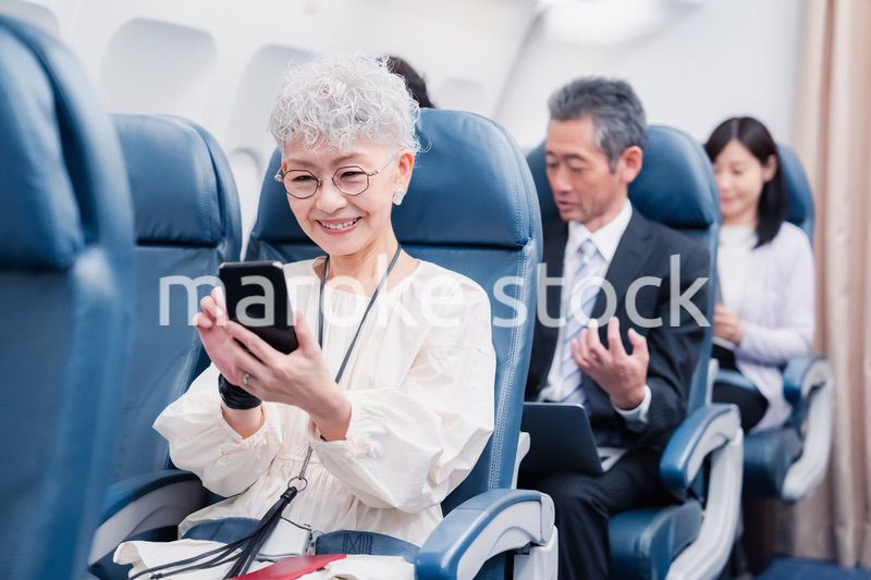 飛行機でスマホを使うシニア女性