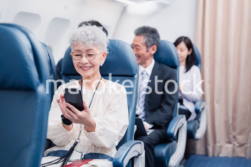 飛行機でスマホを使うシニア女性