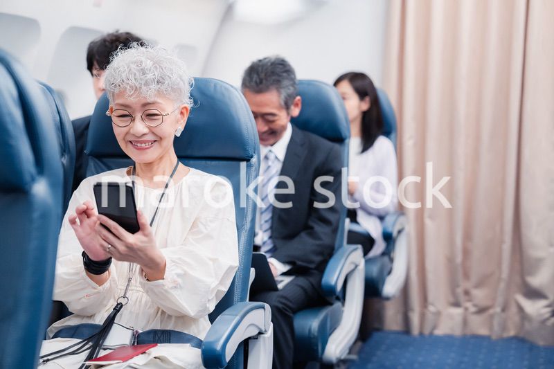 飛行機でスマホを使うシニア女性