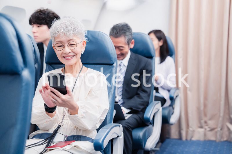 飛行機でスマホを使うシニア女性