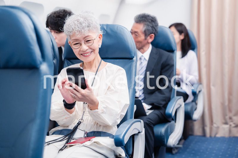 飛行機でスマホを使うシニア女性