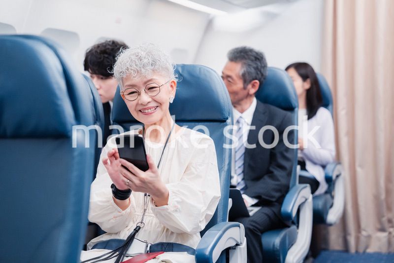 飛行機でスマホを使うシニア女性