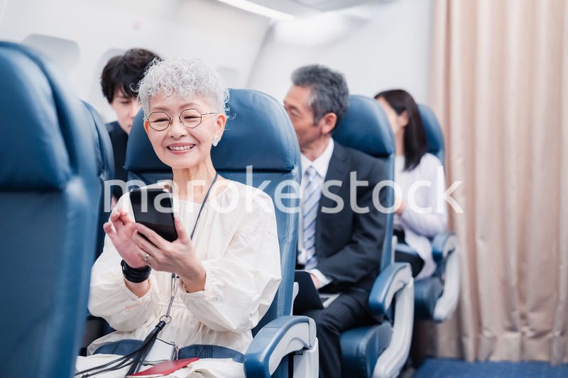飛行機でスマホを使うシニア女性