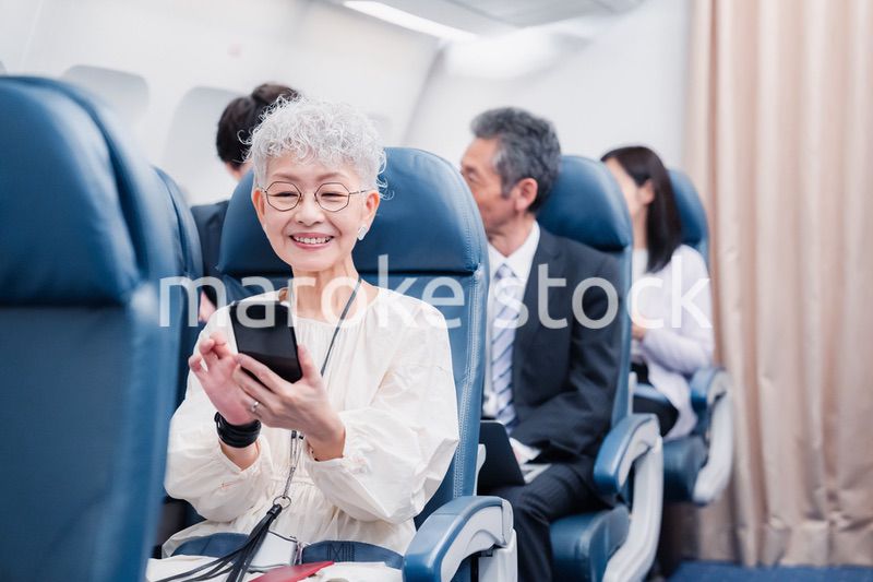 飛行機でスマホを使うシニア女性