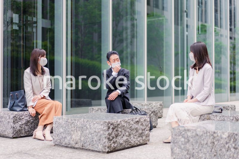 マスクをしてオフィスで立ち話をするビジネスパーソン