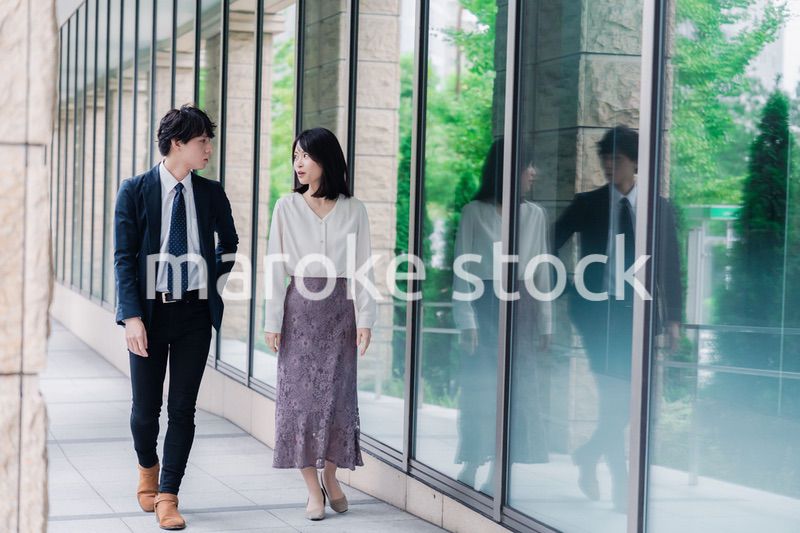 話しながらオフィスを歩く男女のビジネスパーソン