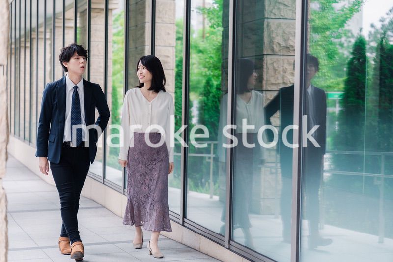 話しながらオフィスを歩く男女のビジネスパーソン
