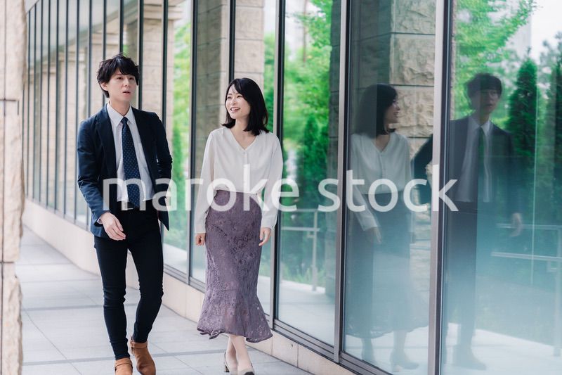 話しながらオフィスを歩く男女のビジネスパーソン