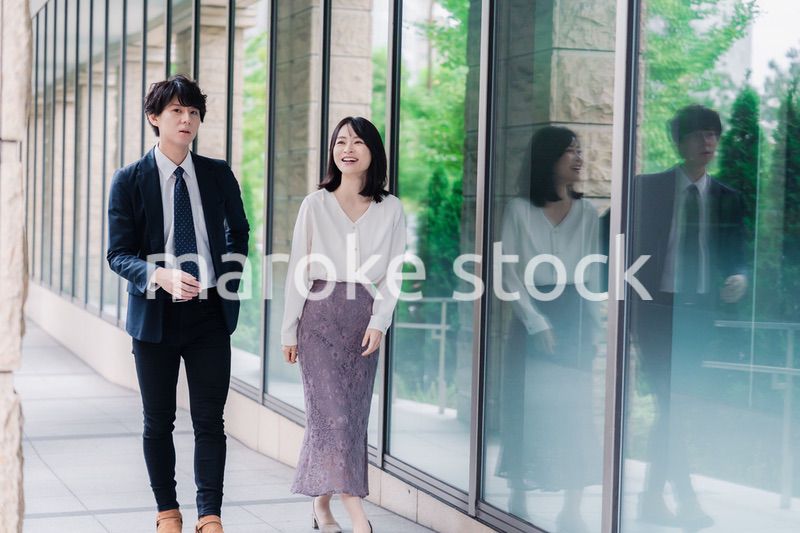 話しながらオフィスを歩く男女のビジネスパーソン