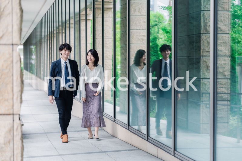 話しながらオフィスを歩く男女のビジネスパーソン