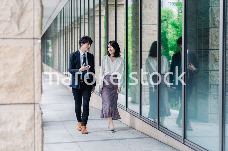 話しながらオフィスを歩く男女のビジネスパーソン