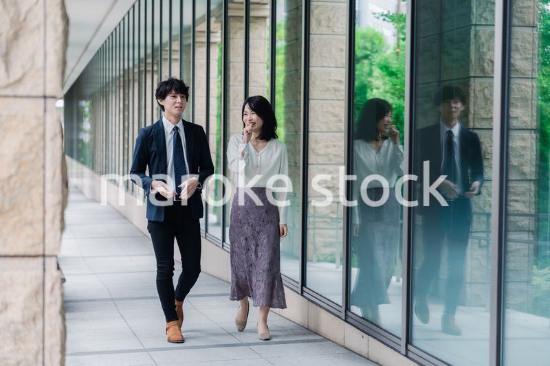 話しながらオフィスを歩く男女のビジネスパーソン