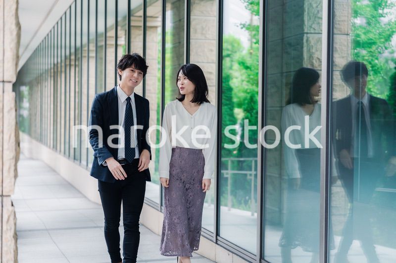 話しながらオフィスを歩く男女のビジネスパーソン
