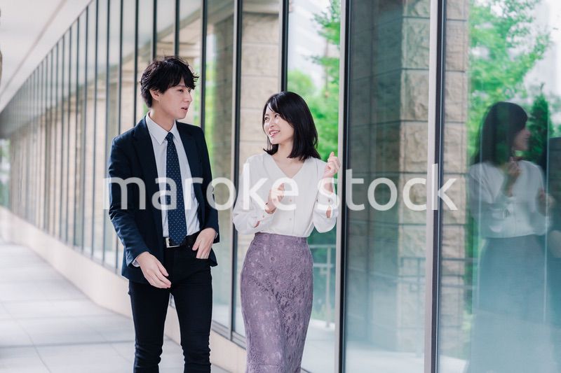 話しながらオフィスを歩く男女のビジネスパーソン