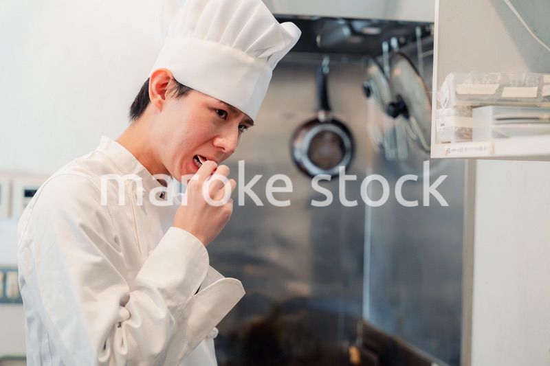 厨房で味見をする男性のシェフ