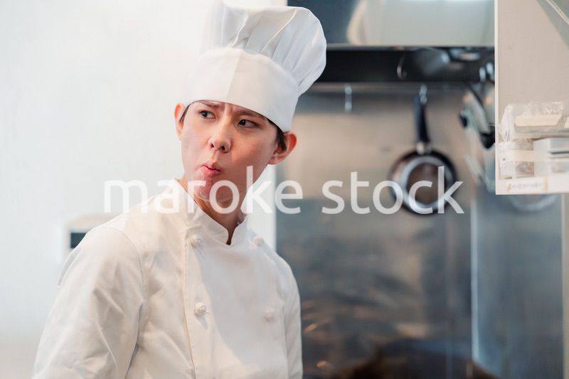 厨房で味見をする男性のシェフ