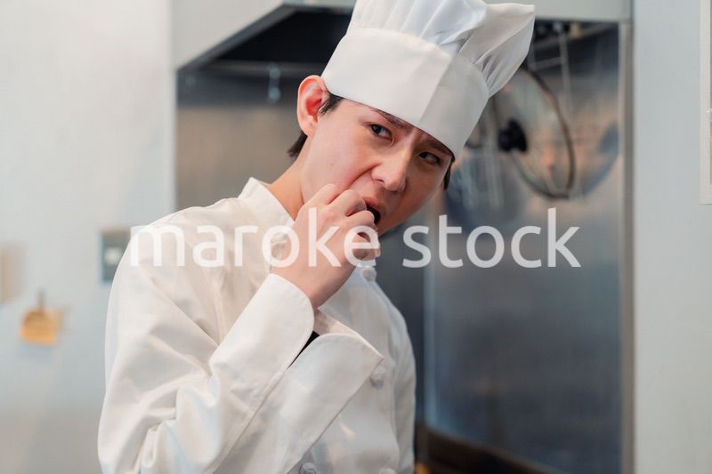 厨房で味見をする男性のシェフ
