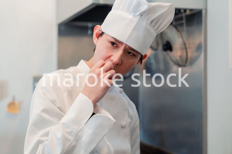 厨房で味見をする男性のシェフ