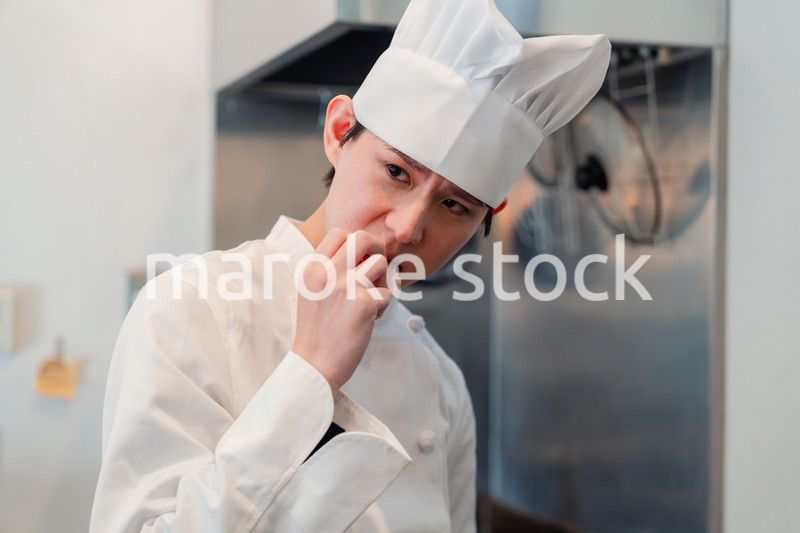 厨房で味見をする男性のシェフ