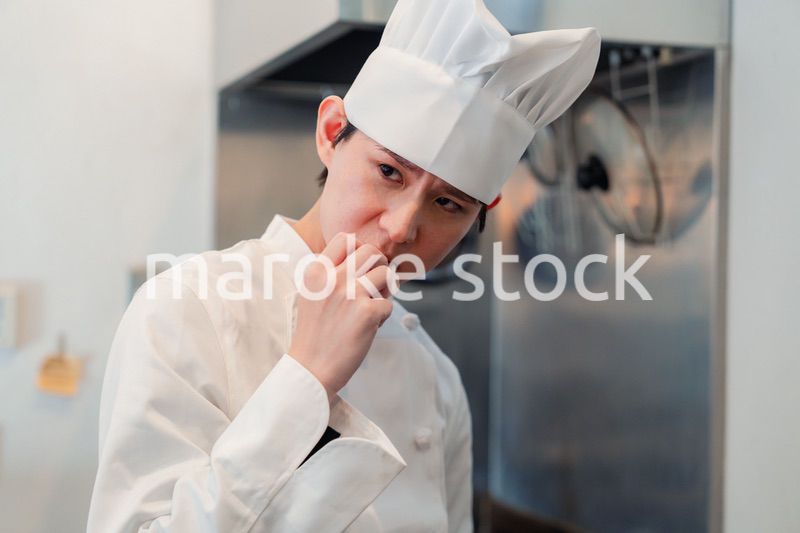 厨房で味見をする男性のシェフ