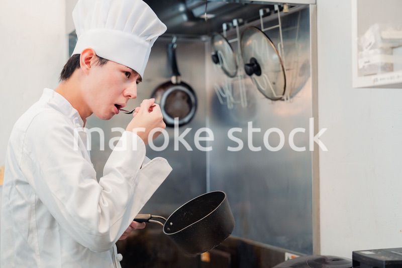 厨房で味見をする男性のシェフ