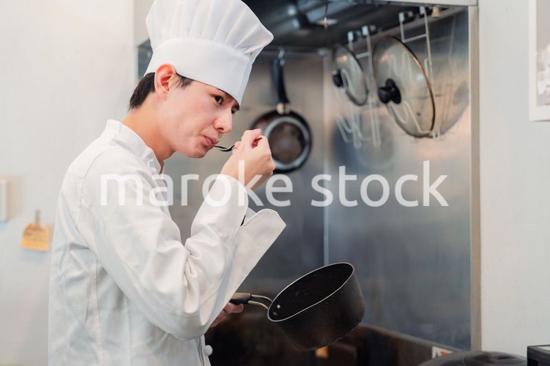 厨房で味見をする男性のシェフ