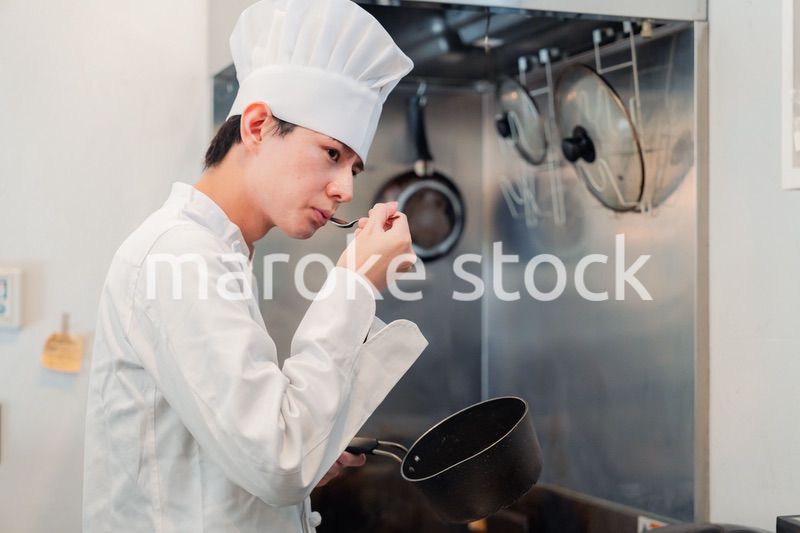 厨房で味見をする男性のシェフ