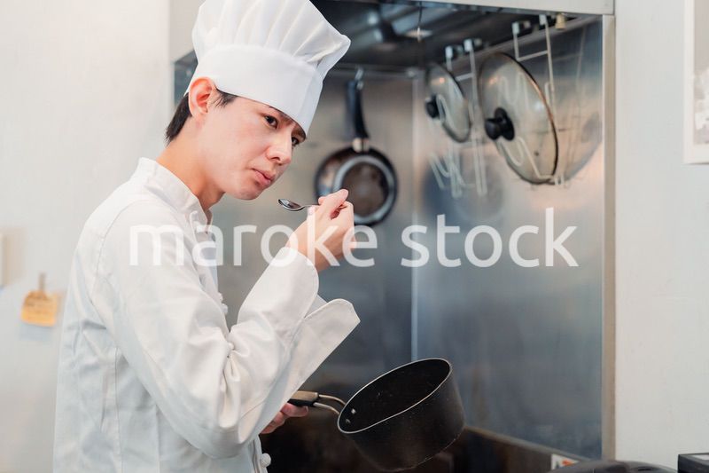 厨房で味見をする男性のシェフ