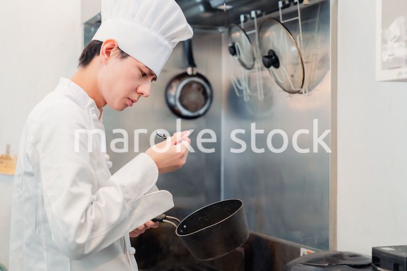 厨房で味見をする男性のシェフ