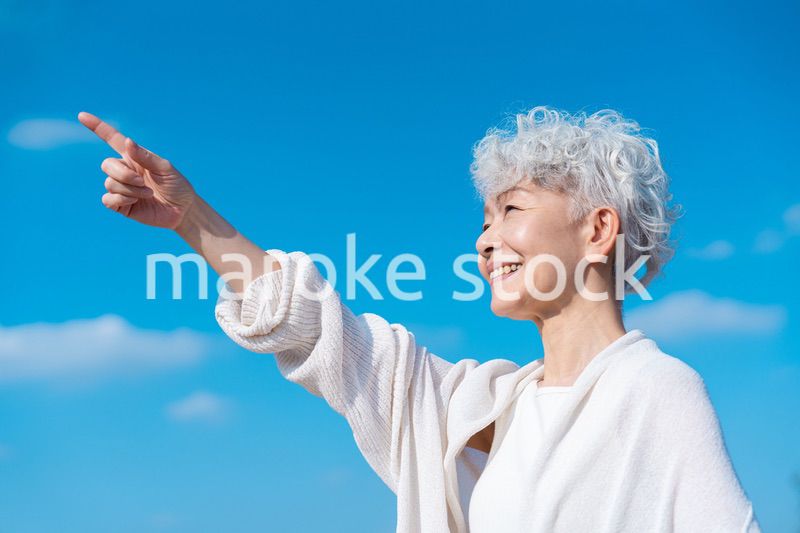 青空の下で未来を指差すシニアの女性