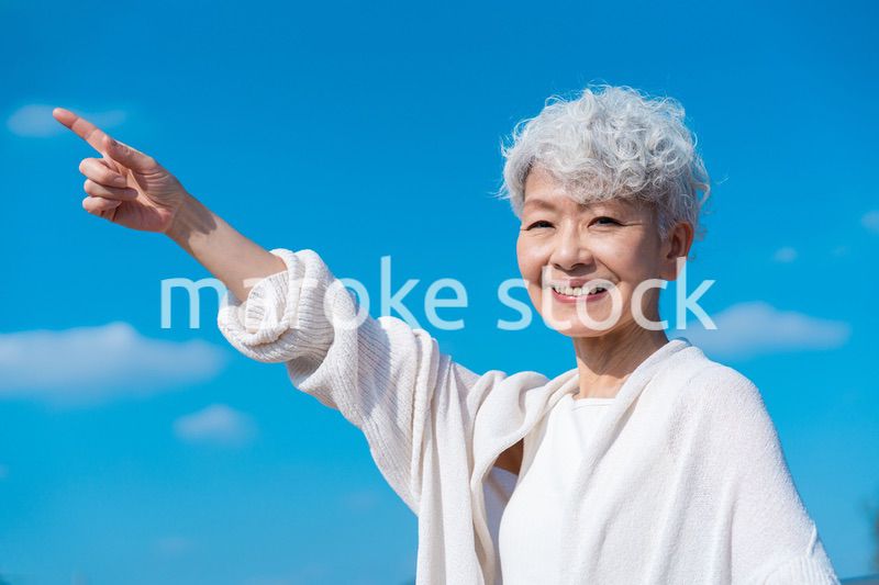 青空の下で未来を指差すシニアの女性