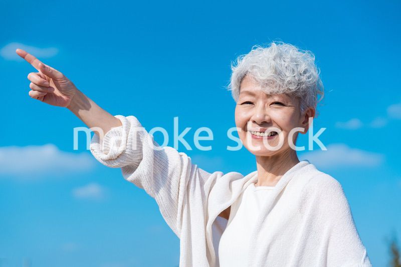 青空の下で未来を指差すシニアの女性
