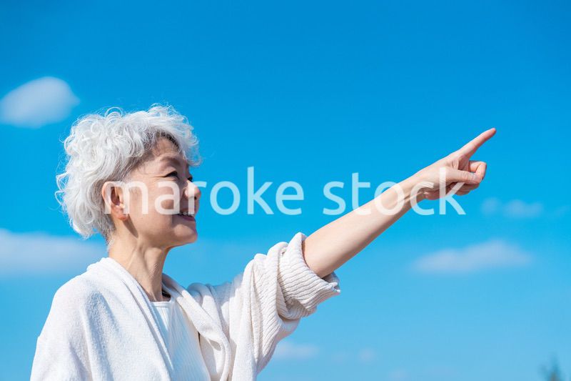 青空の下で未来を指差すシニアの女性