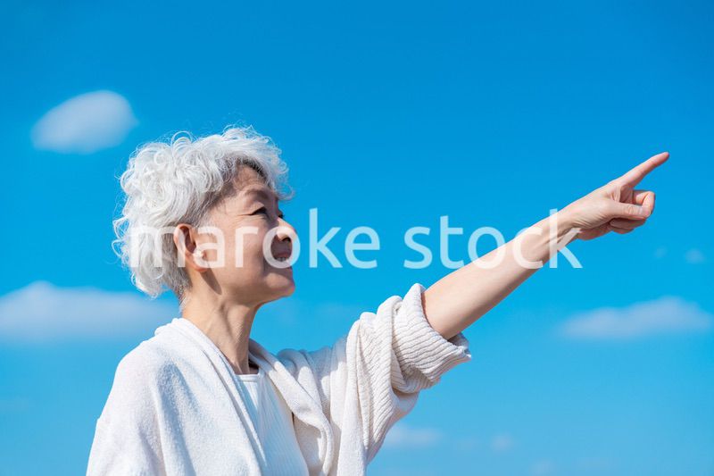 青空の下で未来を指差すシニアの女性