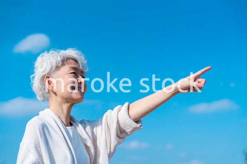 青空の下で未来を指差すシニアの女性