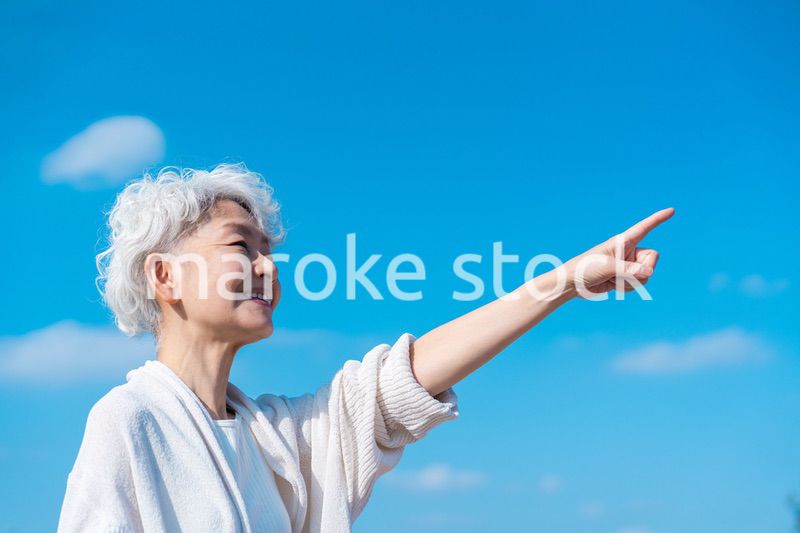 青空の下で未来を指差すシニアの女性