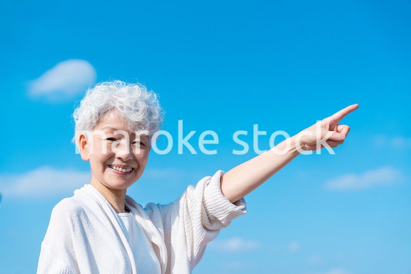 青空の下で未来を指差すシニアの女性