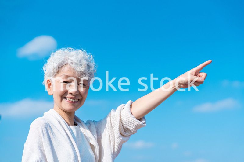 青空の下で未来を指差すシニアの女性